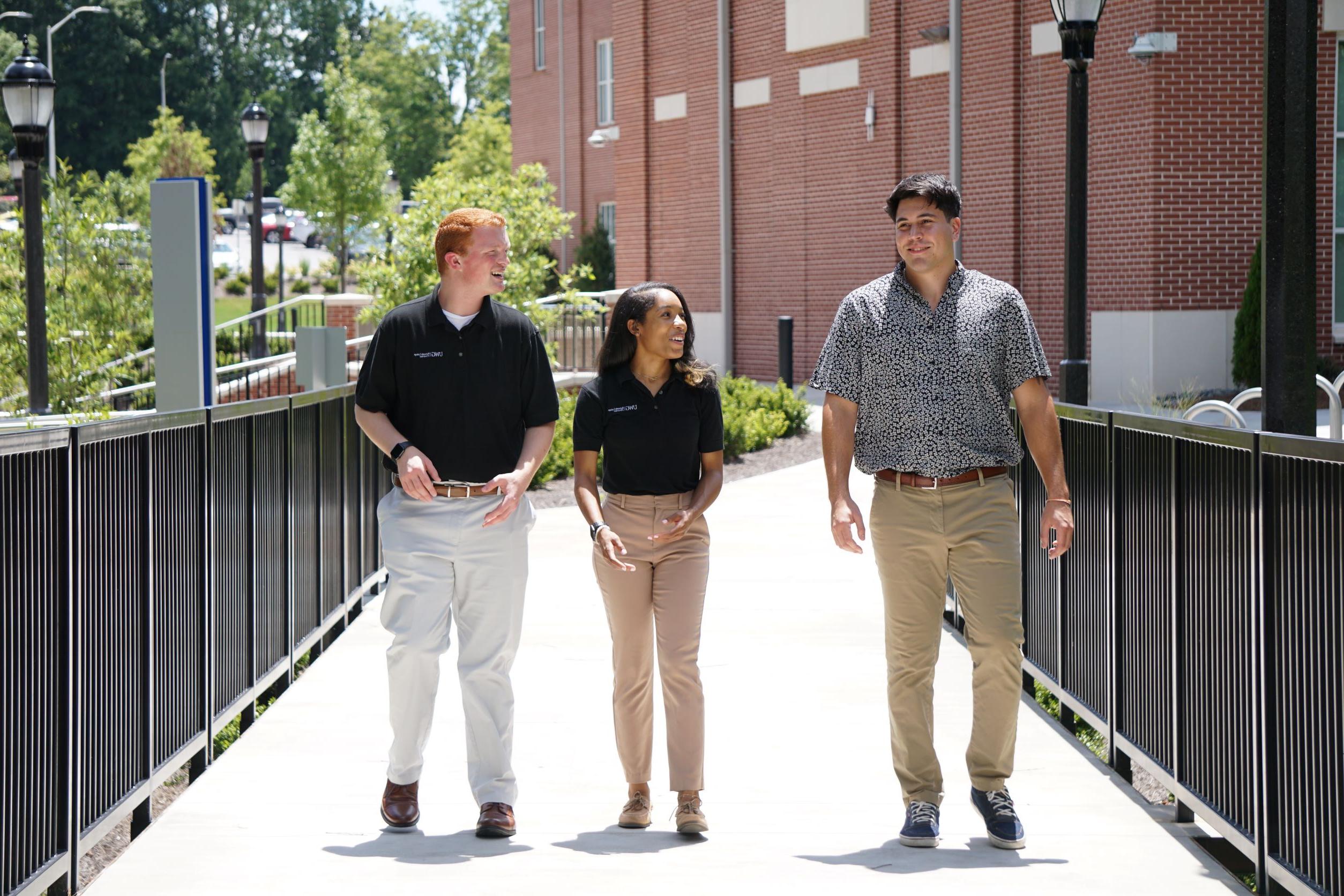 Three business students in professional dress walking across the bridge outside of the College of Business.